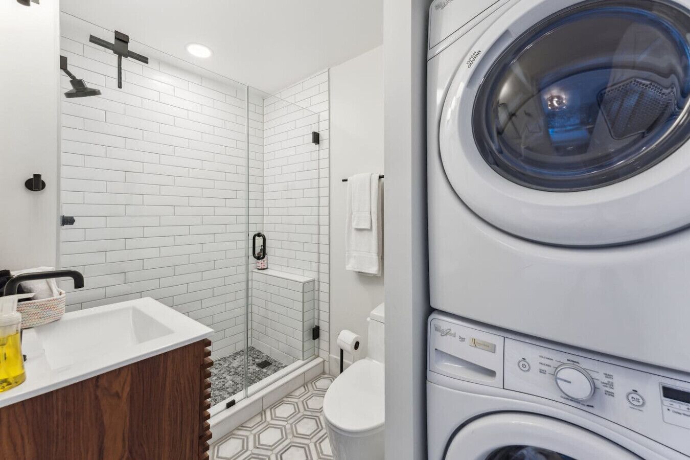 A modern bathroom with a shower, toilet, and stacked washing machines.