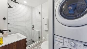 A modern bathroom with a shower, toilet, and stacked washing machines.