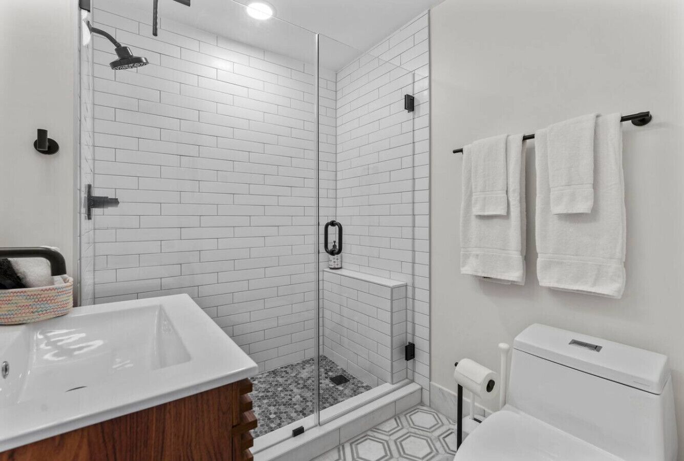 Een moderne badkamer met een douchecabine van glas, witte betegelde wanden, een witte wastafel en een toilet.