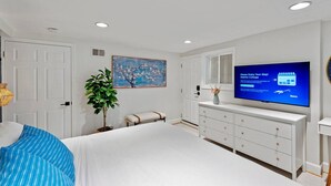 Ein Schlafzimmer mit Bett, Fernseher, Kommode, Sitzbank und Gemälde.