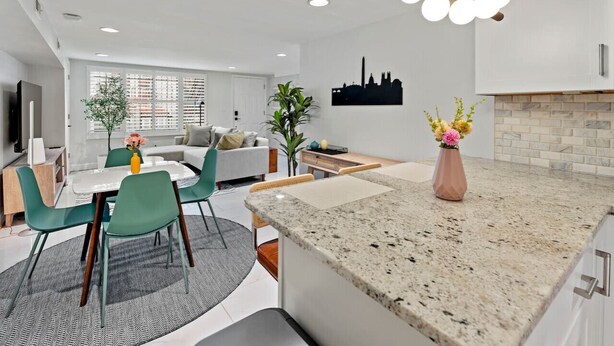 Eine moderne Küche mit Granitarbeitsplatten, ein Essbereich mit grünen Stühlen und ein Wohnzimmer mit Sofa und Fernseher.