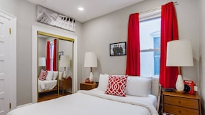A hotel room with a large bed, two bedside tables with lamps, a wardrobe, and a window with red curtains. - Mid-Century Marvel Steps from Restaurants and Bars (Washington)