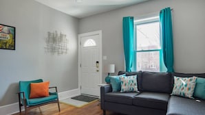 A living room with a dark grey sofa, teal curtains, and a teal chair with an orange cushion. - Mid-Century Marvel Steps from Restaurants and Bars (Washington)