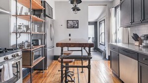 Une cuisine avec une table en bois au centre, des étagères en métal, une cuisinière et un lave-vaisselle.
