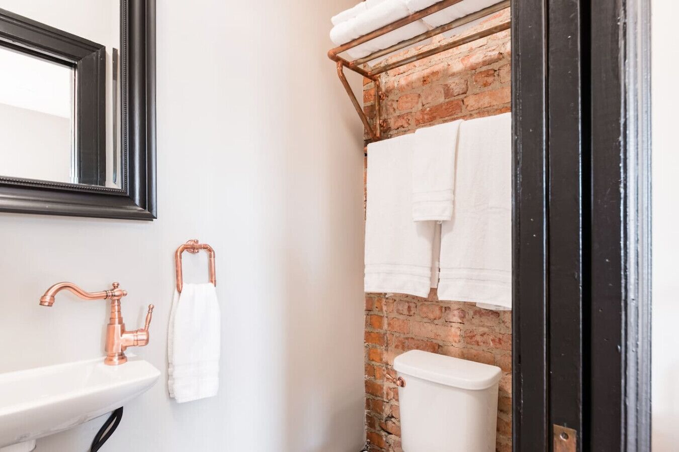 A bathroom with a white sink, copper faucet, and a white toilet. There is a towel hanging on a copper towel rack.