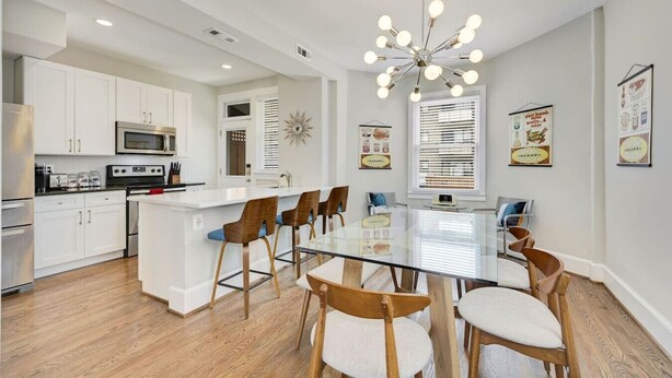 Een moderne keuken met witte kasten, een centraal eiland en een eethoek met een tafel met glazen blad en houten stoelen.