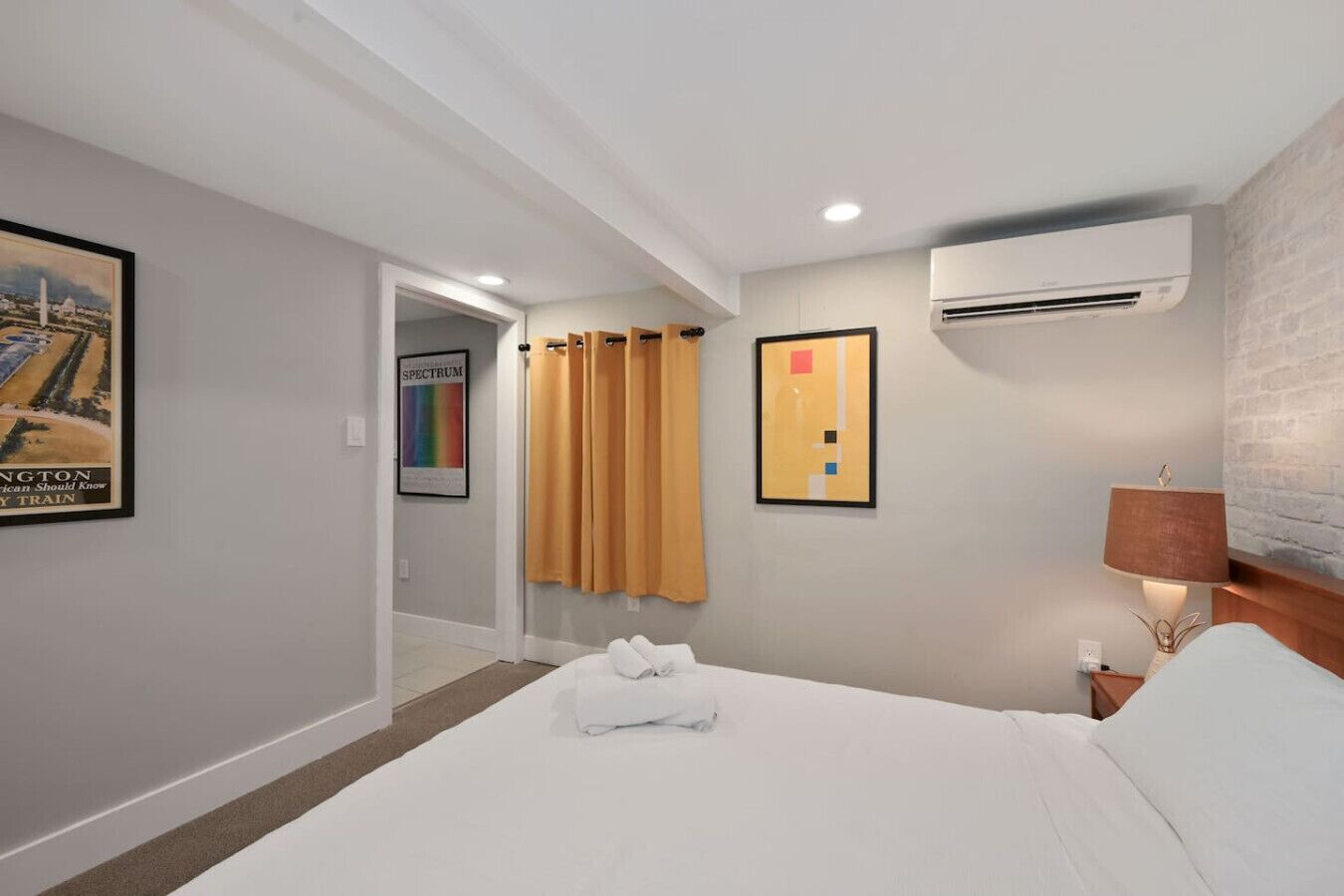 Ein Hotelzimmer mit Bett, Nachttisch, Klimaanlage, Lampe und einem Bild an der Wand.