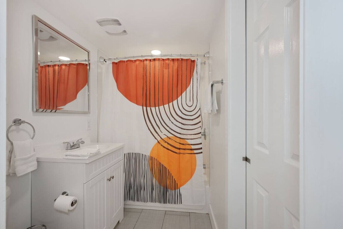 Une salle de bain avec un meuble-lavabo blanc, un miroir, des toilettes et un rideau de douche à motifs géométriques.