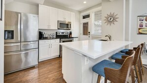 A modern kitchen with stainless steel appliances, white cabinetry, and a central island with bar stools. - Massive Mid-Century Marvel: 5 Bedrooms and Parking (Washington)
