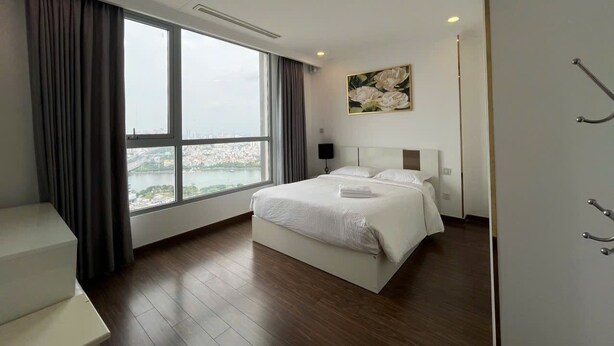 A modern hotel room with a large bed, a view of a cityscape through a large window, and a minimalist design.