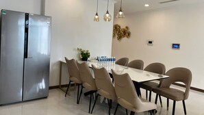 A modern dining area with a stainless steel refrigerator, a marble-top table, beige chairs, and hanging pendant lights.