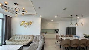 A modern living room with a sofa, a dining table with chairs, and a kitchen area in the background.