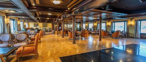 A spacious lobby with wooden flooring, multiple seating areas with chairs, and large windows providing natural light.