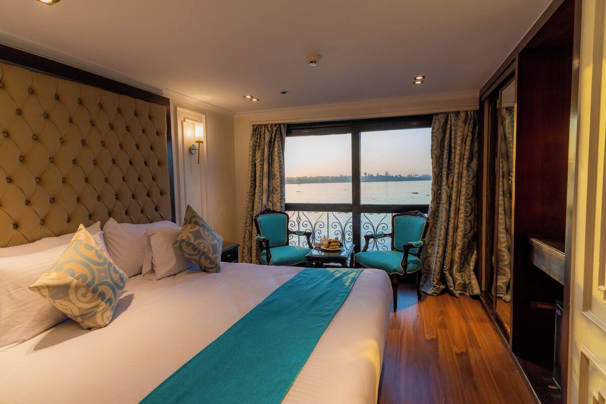 A hotel room with a large bed, a view of the water, and a balcony with chairs.