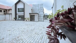 Un edificio moderno con fachada geométrica, patio empedrado y plantas en macetas.