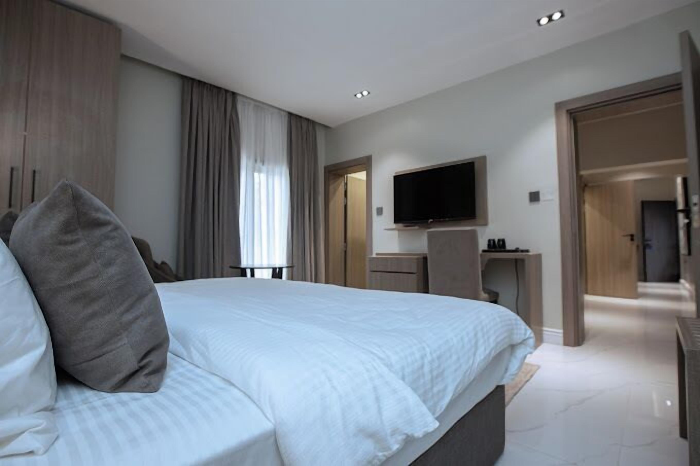 A modern hotel room with a large bed, a desk with a flat-screen TV, and a walk-in closet.