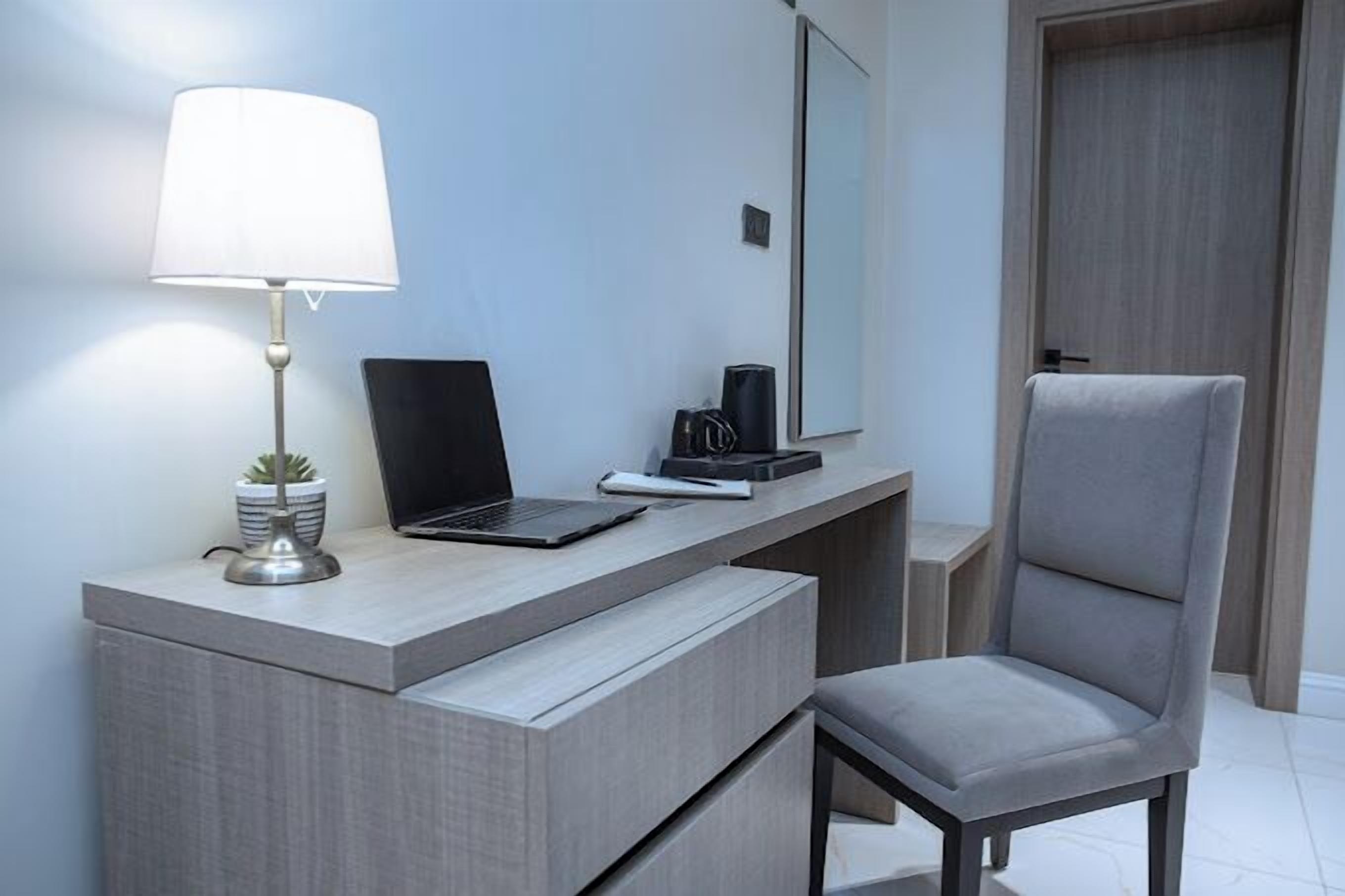 Una habitación de hotel moderna con escritorio, laptop, lámpara y una silla.