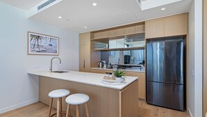 Une cuisine moderne avec des meubles en bois, un réfrigérateur en acier inoxydable et un plan de travail blanc.