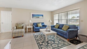 A living room with a striped armchair, two blue sofas, a white coffee table, and a patterned rug. - Spacious 4-bedroom house with 2 master suites in lovely Port Charlotte. (Port Charlotte)