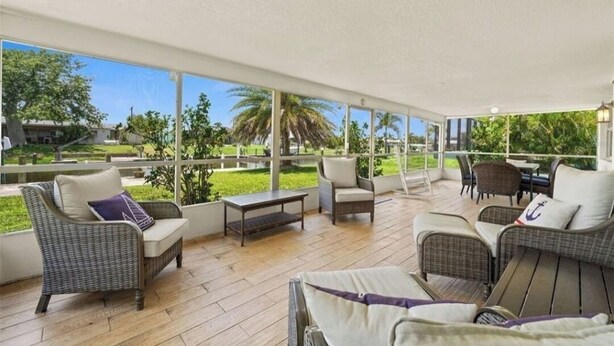 A covered outdoor seating area with wicker furniture, a table, and a view of the surrounding greenery and buildings. - Spacious 4-bedroom house with 2 master suites in lovely Port Charlotte. (Port Charlotte)