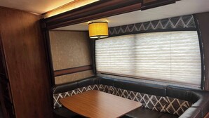 A cozy RV interior with a wooden table, cushioned seating, and a window with blinds. - Ample Lakeside Travel Trailer (Bridgeport)