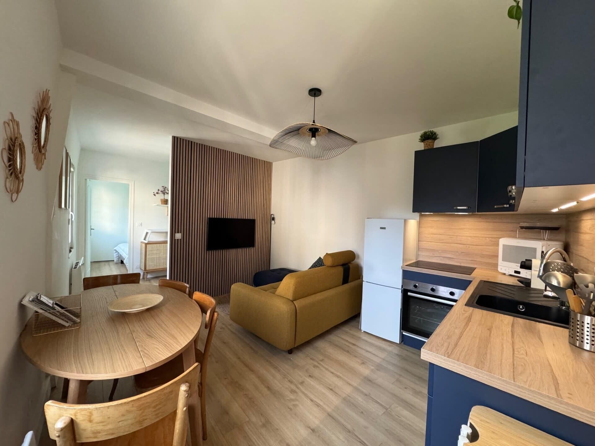 A compact living space with a dining area, sofa, kitchenette, and a TV mounted on the wall.