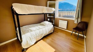 A bunk bed in a room with a wooden floor, a window with a view of a mountain, and a chair. - Charming T3 with balcony in the heart of Briançon (Briançon)