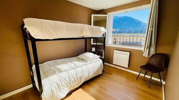 A bunk bed in a room with a wooden floor, a window with a view of a mountain, and a chair.