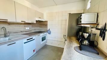 A modern kitchen with white cabinets, a built-in oven, a microwave, and a coffee maker.