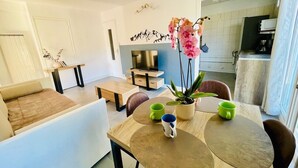 A modern living room with a sofa, a dining table with chairs, a TV, and a kitchen area in the background. - Charming T3 with balcony in the heart of Briançon (Briançon)