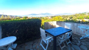 Un patio exterior con mesa y sillas, con vistas a un paisaje pintoresco con colinas y una lejana vista al mar.