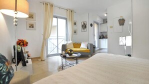 A modern hotel room with a large bed, a sofa, a dining table, and a view of the city.