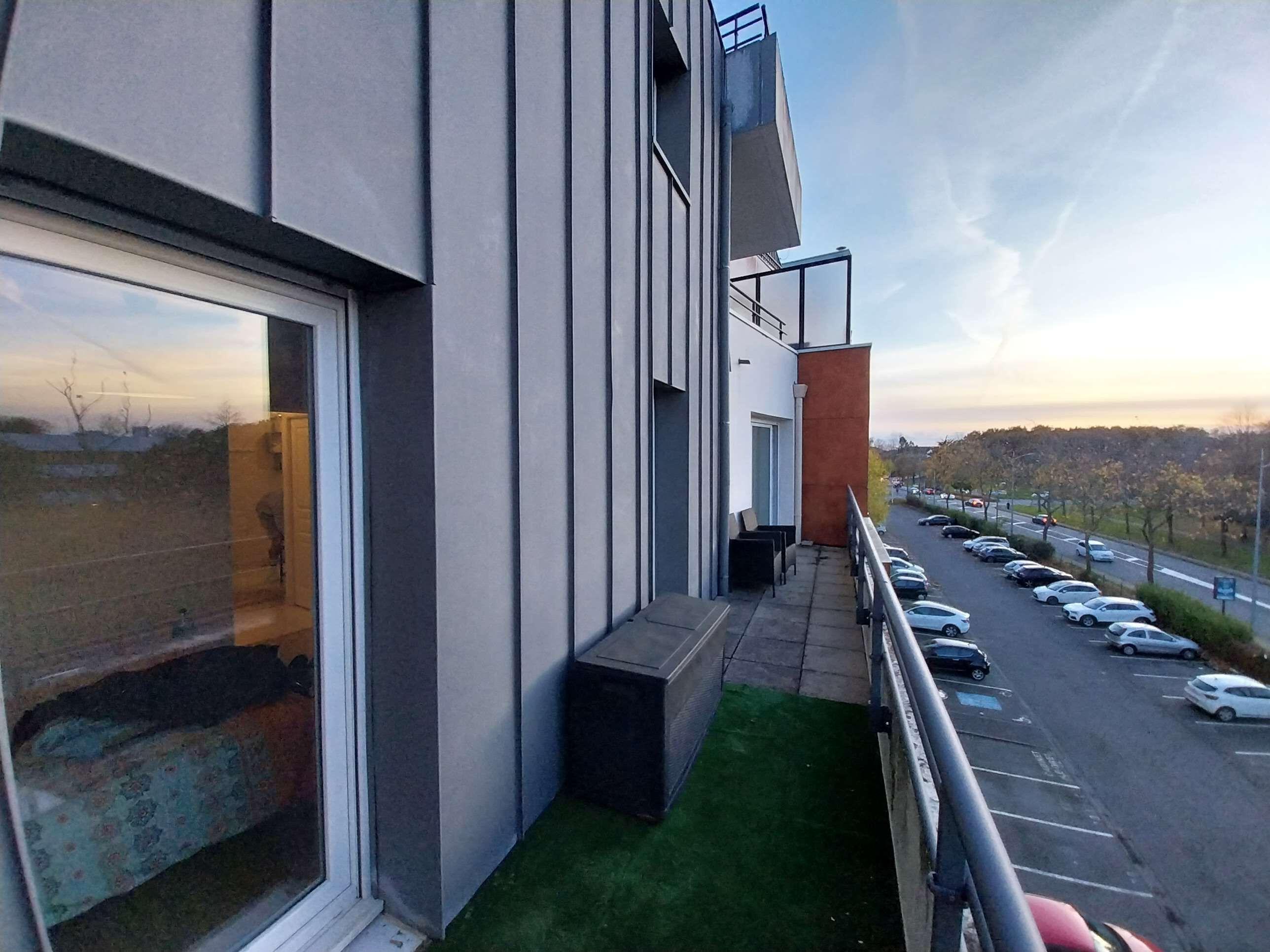 Un bâtiment moderne doté d’un balcon donnant sur un parking et une route.