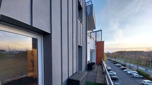 A modern building with a balcony overlooking a parking lot and a road. - Charming T3 with balcony near beach (Vannes)