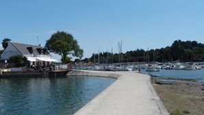 A marina with boats docked, a building named 'LE CORLAZO' with outdoor seating, and a clear sky. - Charming T3 with balcony near beach (Vannes)