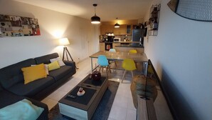 A modern living room with a sofa, coffee table, and a dining area with chairs. - Charming T3 with balcony near beach (Vannes)