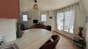 A modern kitchen with a dining area, a TV, and large windows with curtains. - Bourgeois apartment (Trouville-sur-Mer)