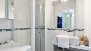 A modern bathroom with a glass-enclosed shower, a white sink with a mirror above it, and a toilet. - Bourgeois apartment (Trouville-sur-Mer)