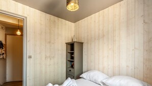A bedroom with a wooden wall, a bed with white linens, a wardrobe, and a hanging light fixture. - Bourgeois apartment (Trouville-sur-Mer)