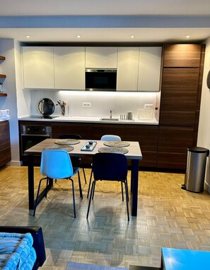 A modern kitchen with built-in appliances, a dining area with a table and chairs, and a herringbone-patterned floor. - Charming T2 with balcony near the Bastille (Paris)