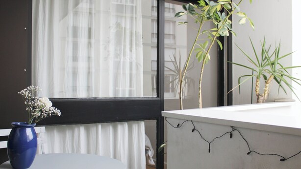 A balcony with a table, a blue vase with flowers, and two potted plants.