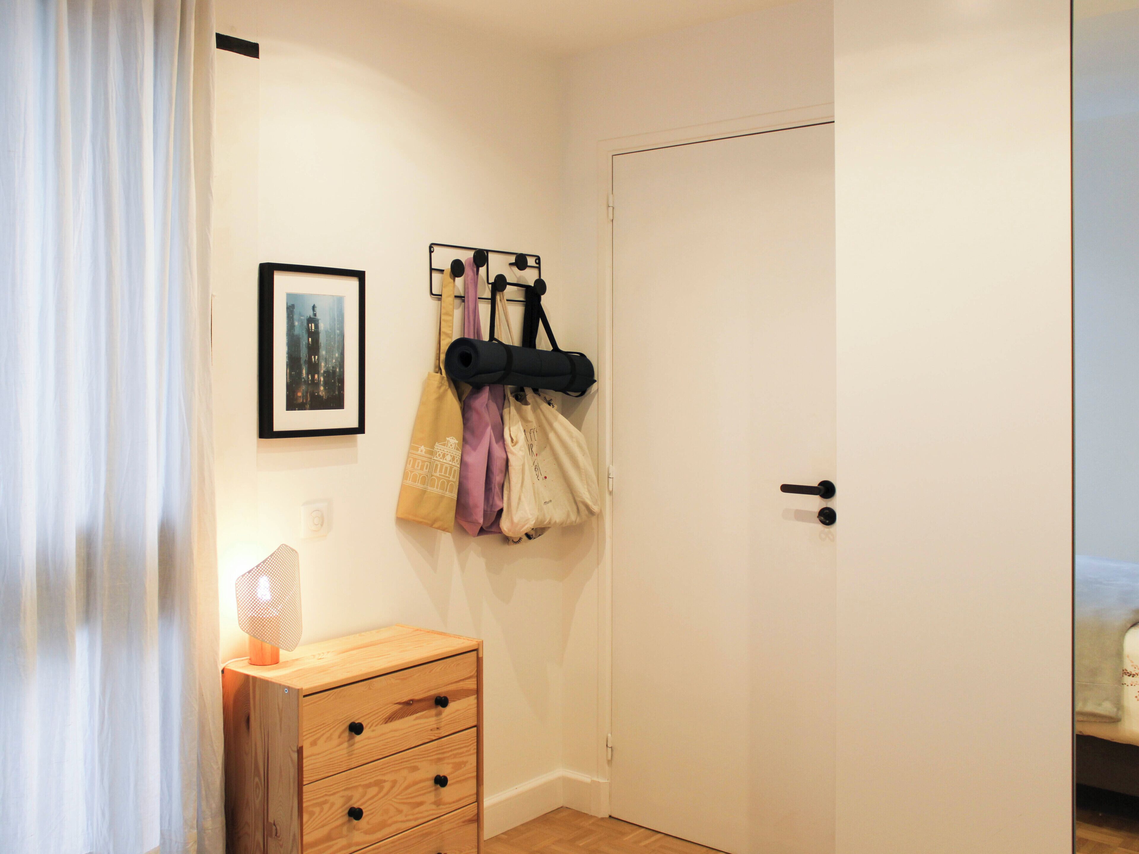 A room with a wooden dresser, a door, and a wall-mounted bag rack with bags.