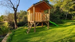 A wooden playhouse with a slide, surrounded by a well-maintained lawn and trees. - Spacious villa with pool and bay views (Le Castellet)