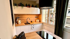 Une cuisine de taille réduite, dotée d’un plan de travail en bois, d’un évier noir et d’une fenêtre donnant sur des immeubles.