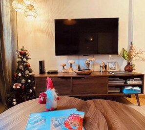 Una sala de estar con televisor de pantalla plana, un árbol de Navidad, una mesa de centro de madera y un peluche.