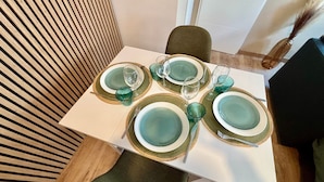 Une table à manger est dressée avec de la vaisselle verte, des verres et des couverts, et est entourée d’une chaise et d’un mur en bois à lattes.