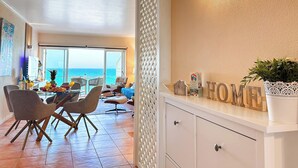 Un salon moderne avec un coin repas, un balcon offrant une vue sur la mer et un luminaire fixé au mur.