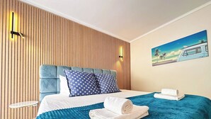 Une chambre d’hôtel avec un lit, une couvre-lit bleue, deux oreillers, une couverture blanche et un tableau au mur.