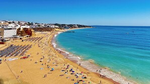 Une plage bordée de rangées de transats et de parasols, une mer d’un bleu limpide et des bâtiments qui s’étendent le long de la côte.