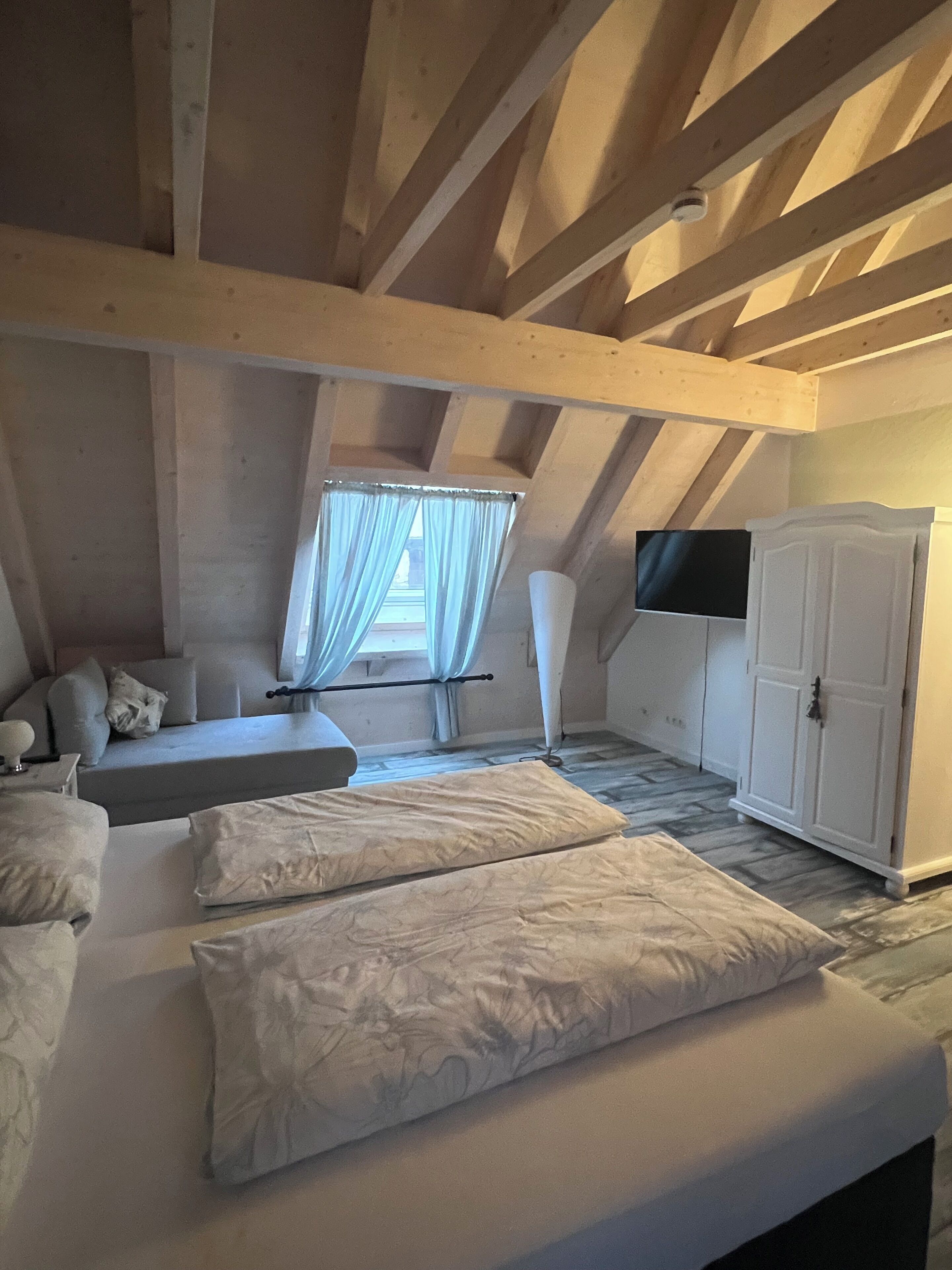 A bedroom with a loft-style ceiling, a bed with white linens, a TV mounted on the wall, and a wardrobe.